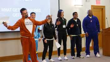 A man in a blue tracksuit enthusiastically leads a group of people in black tracksuits