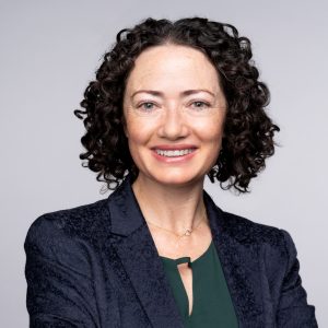 A headshot of Amber Boydstun, a woman in a blue and green suit, smiling at the camera