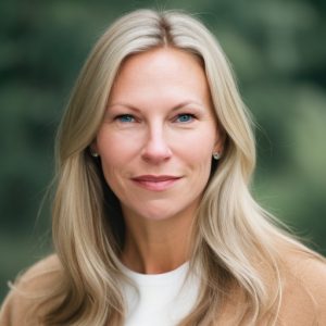 A heashot of Caren Ulrich Stacy, a woman in a tan jacket and white shirt smiling softly at the camera