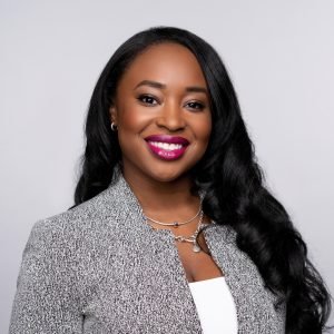 Headshot of Courtney Munnings, a dark-skinned Black woman smiling in magenta lipstick and a black/white speckled blazer.