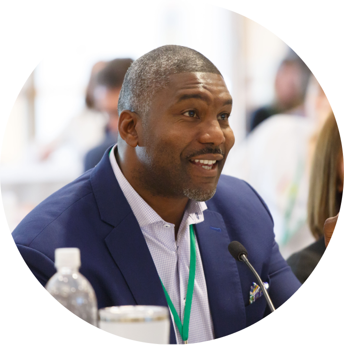 A seated man with a lanyard smiles into a desk microphone