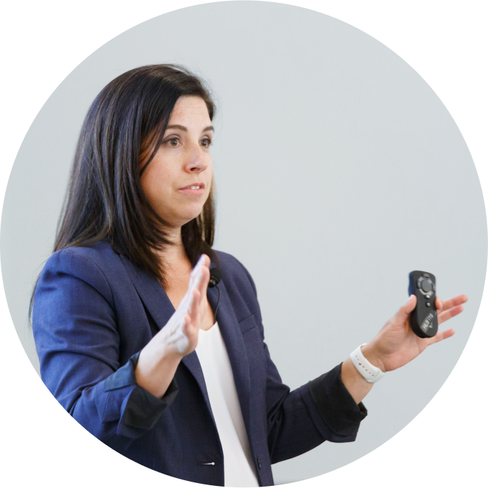 A women speaks on stage, holding a presentation clicker