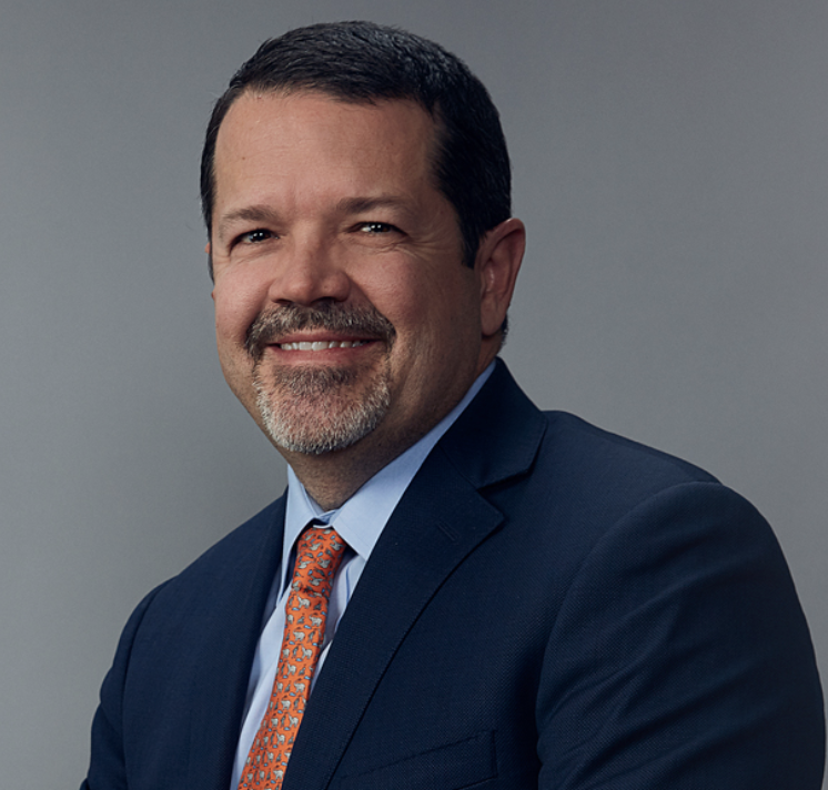 Headshot of Camilo Echavarria, a man with a blue suit and red tie smiling at the camera