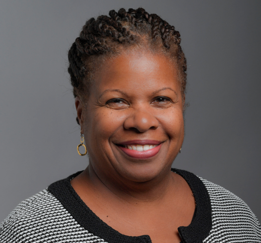 Headshot of Deneen Donnley, a woman with braids and gold earrings smiling at the camera