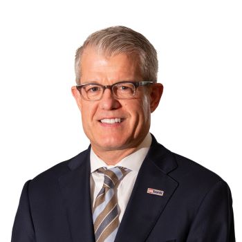 Headshot of Jim Chosy, a man in suit against white background smiling at the camera