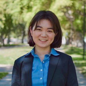 Headshot of Lei Otsuka, an East Asian woman in a blue button-down and black blazer smiling at the camera.