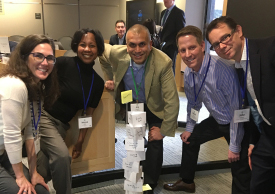 A group of people stand around a tower of index cards and post-it notes